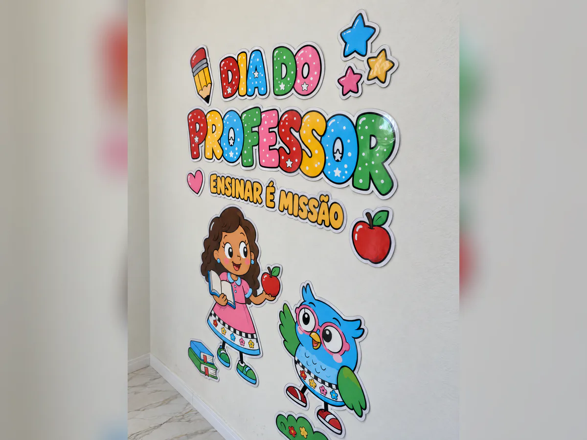 Painel Dia do Professor visto pela direita na parede, mostrando o título colorido, a frase Ensinar é missão, maçã, estrelas, professora e coruja.