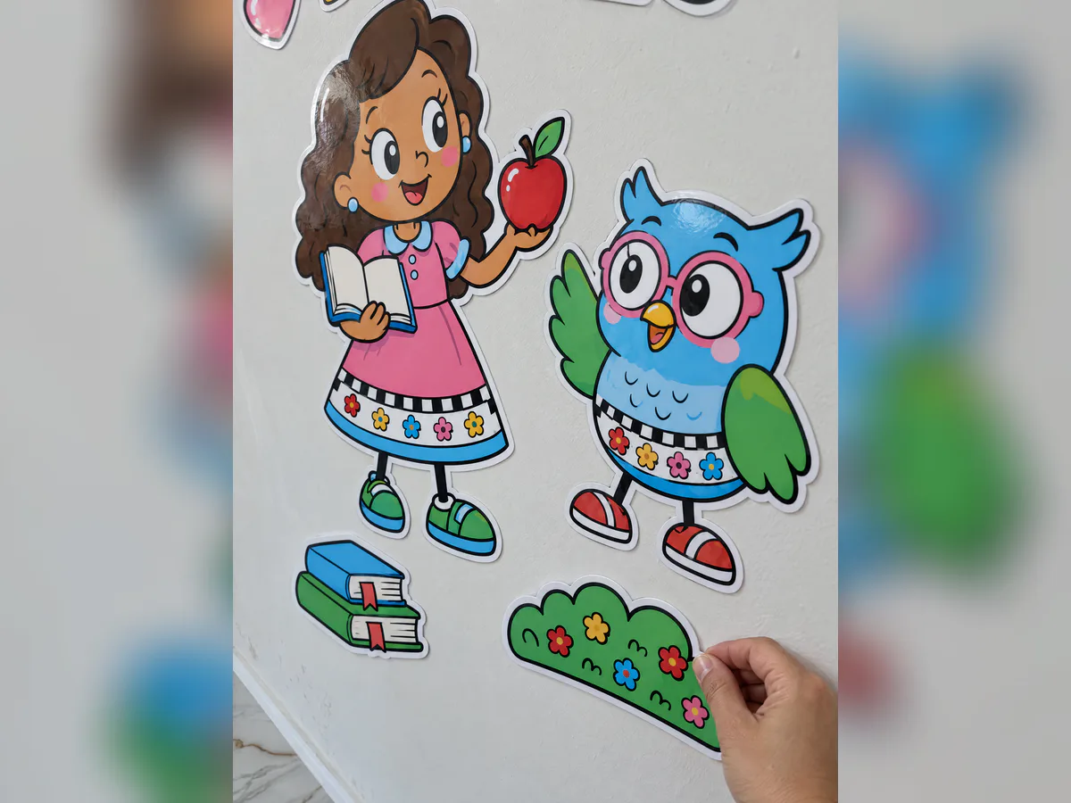 Detalhe do painel na parede com professora segurando livro e maçã, coruja azul, livros no chão e peça decorativa sendo ajustada com a mão.